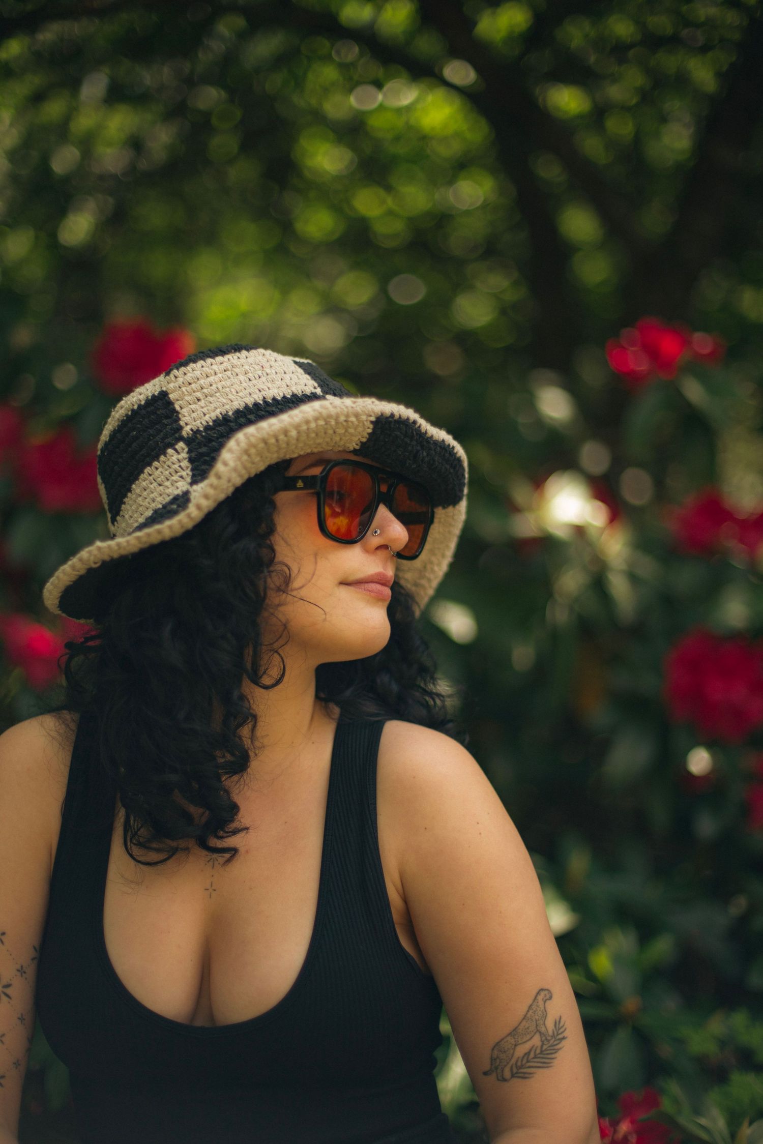 Portrait of a woman with black curly hair with red flowers behind her in a forested background.