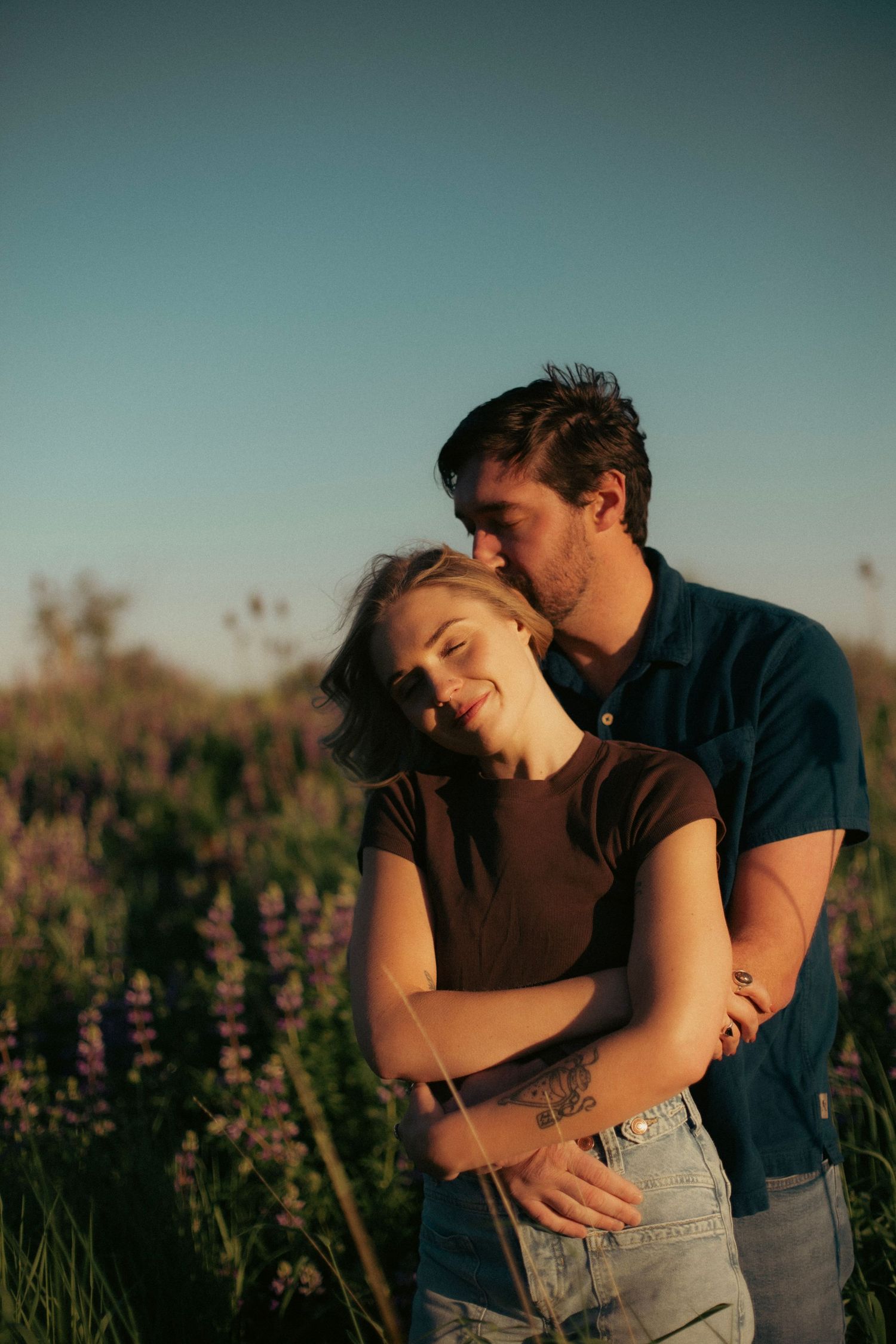 A couple embracing each other in the sun in a grassy field for a couples' photoshoot