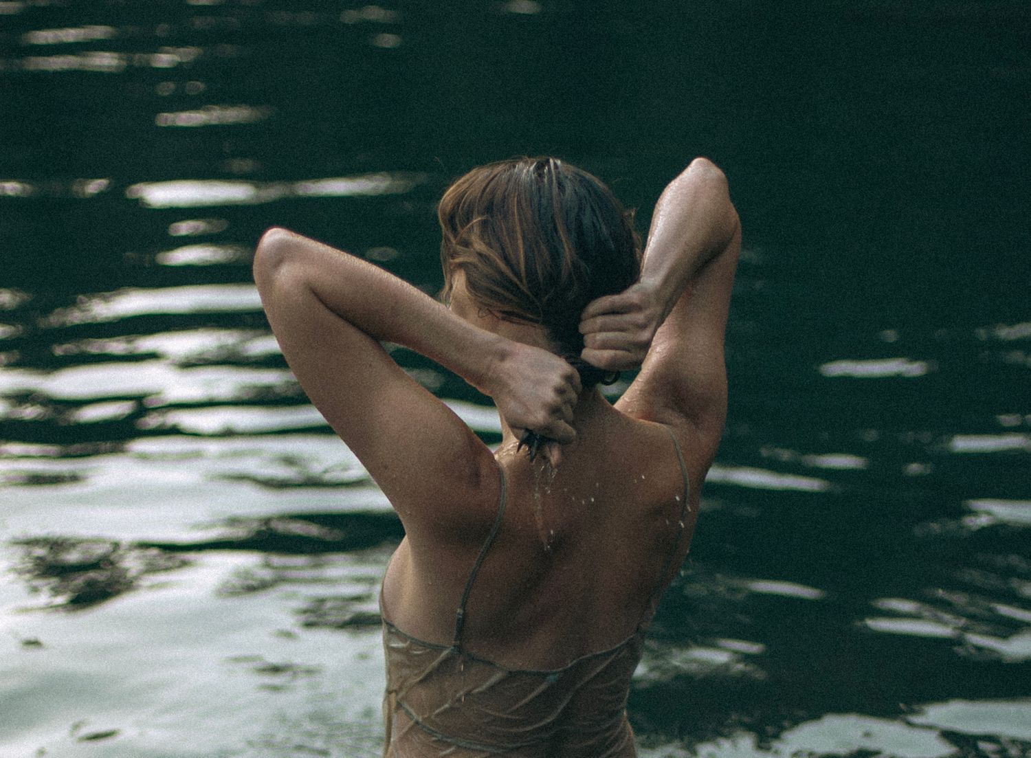 A woman wringing out her hair in a green-tinted lake.