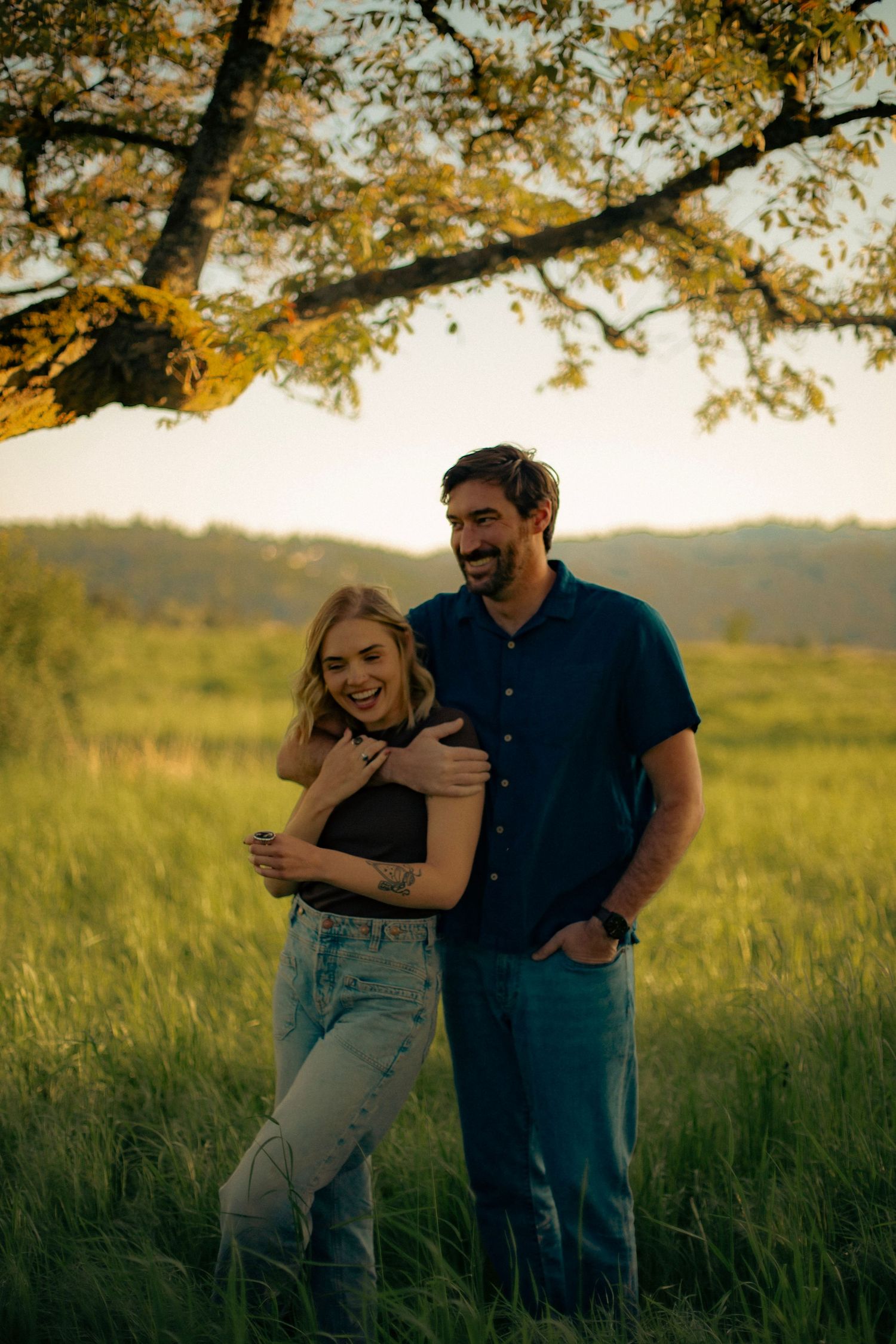 A couple posing and laughing together in a field at sunset