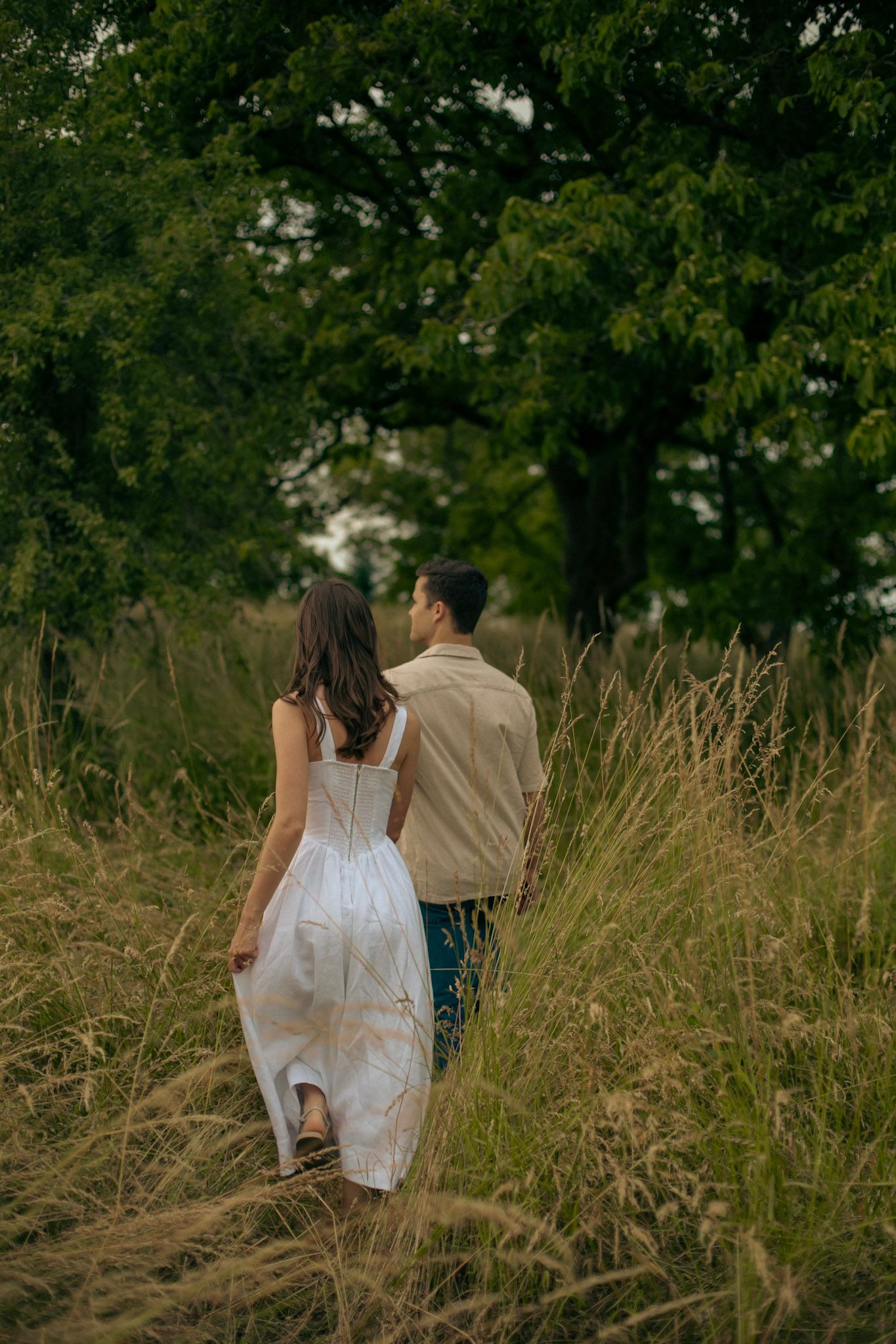 A newly engaged couple walking through tall grass holding hands for an engagement photoshoot in Oregon