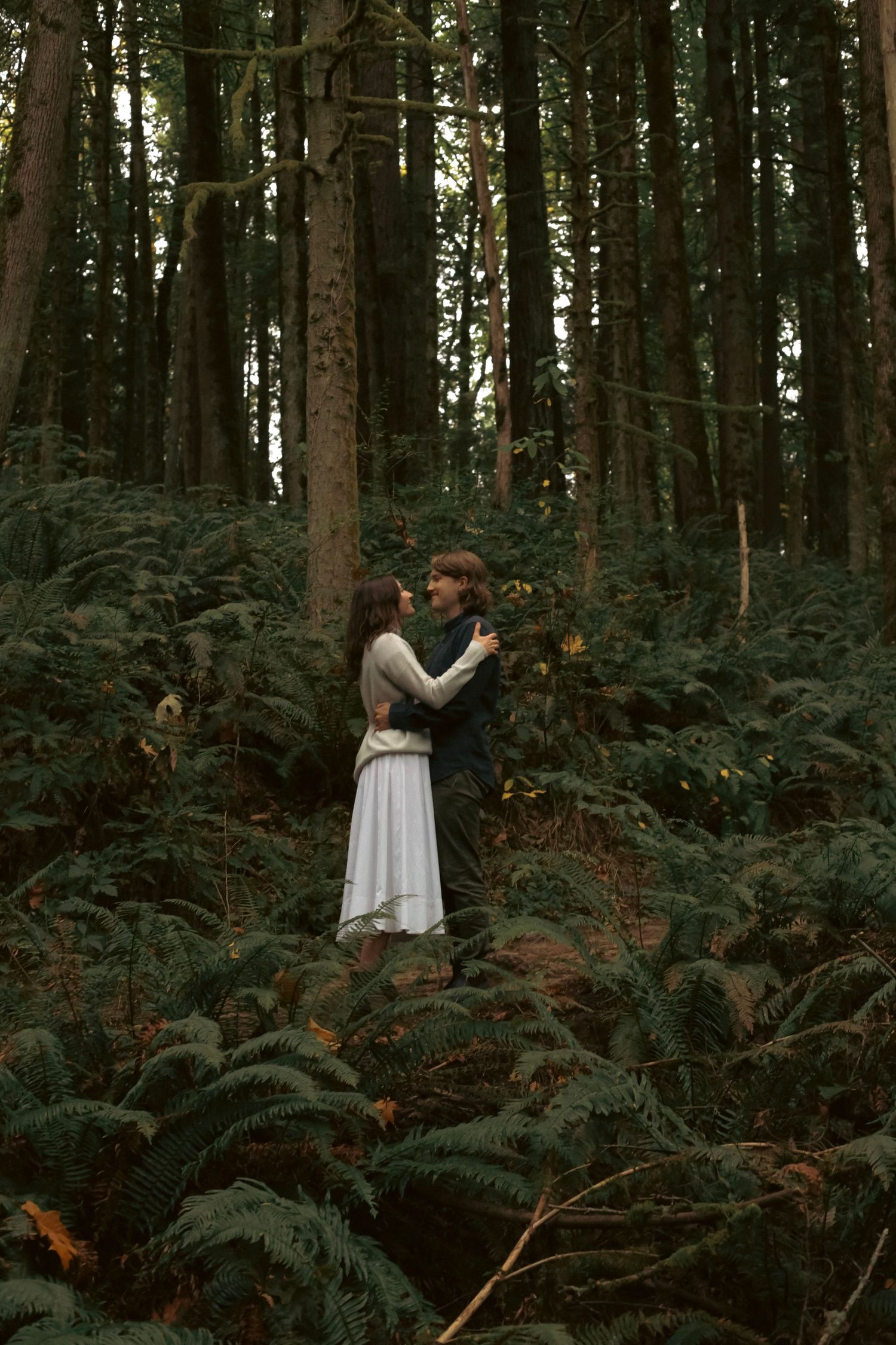 A couple embracing each other in the moody, dark, lush forest for an engagement photoshoot.