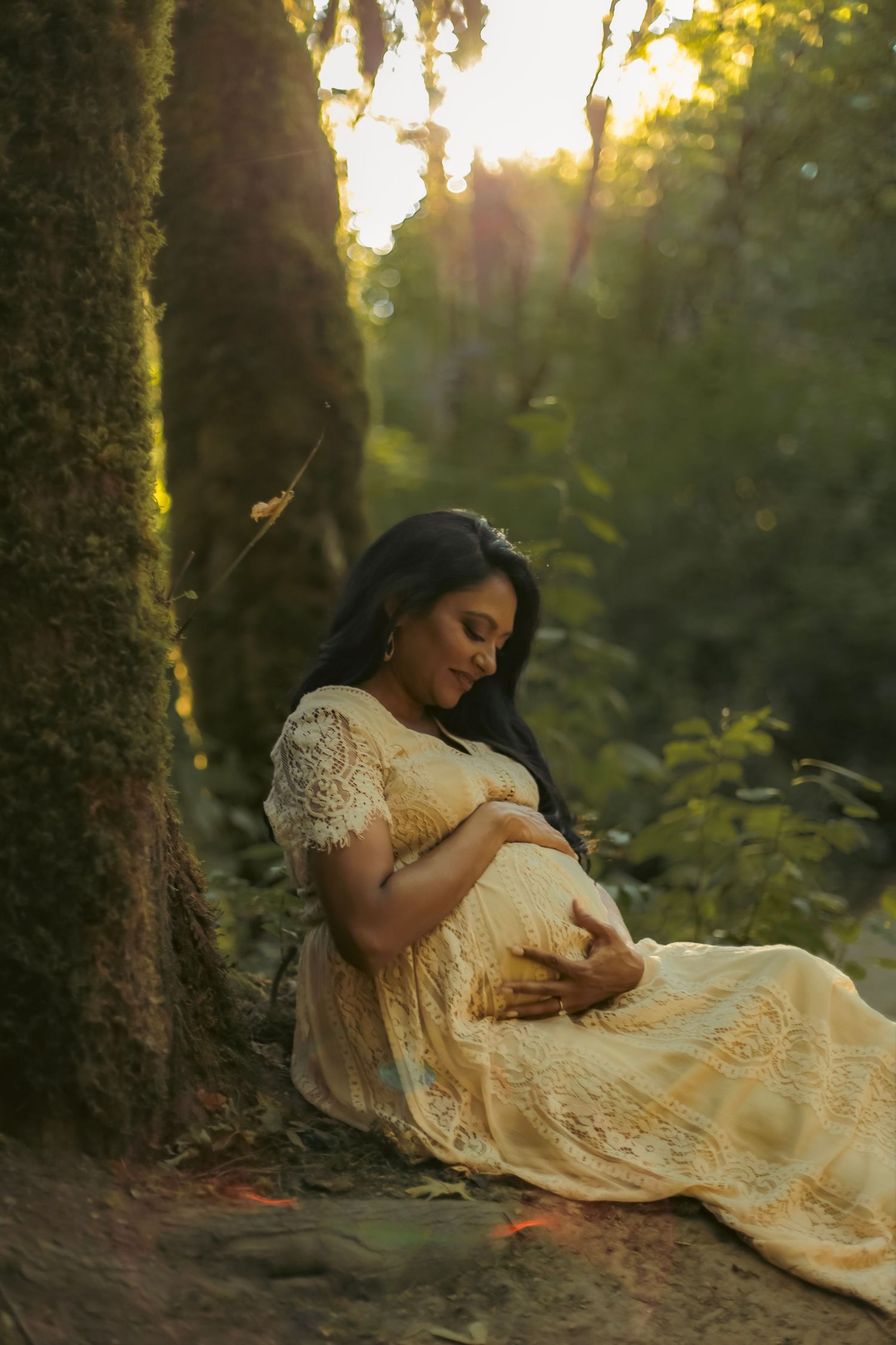 A maternity photoshoot for a mom holding her belly in a white dress amongst trees in a forest