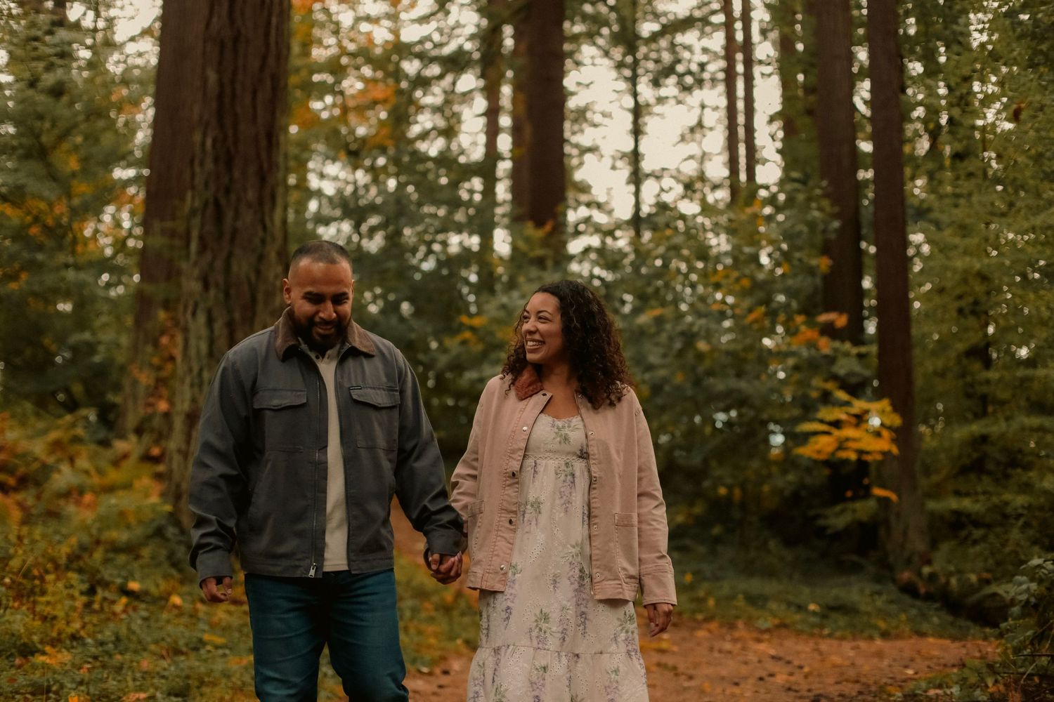 Couple walking in the forest and holding hands smiling at each other.