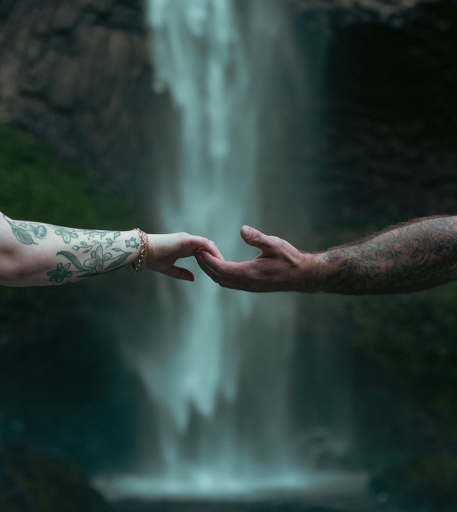 Hands touching romantically in front of a blue Oregon waterfall for an engagement photoshoot