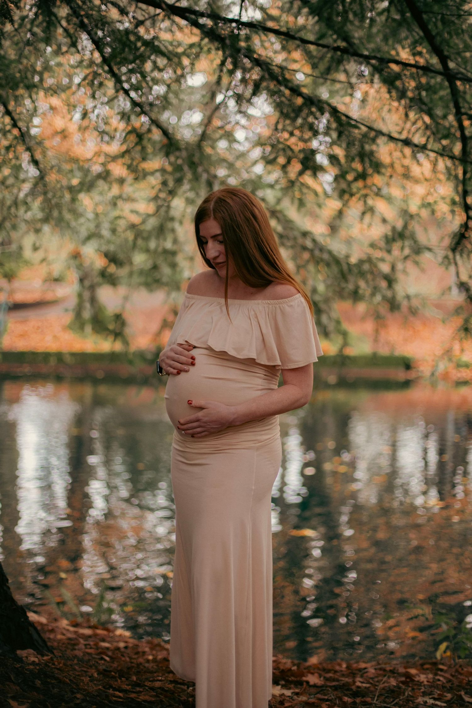 maternity photoshoot for a woman in a pink dress at a portland oregon park with water and leaves in the background