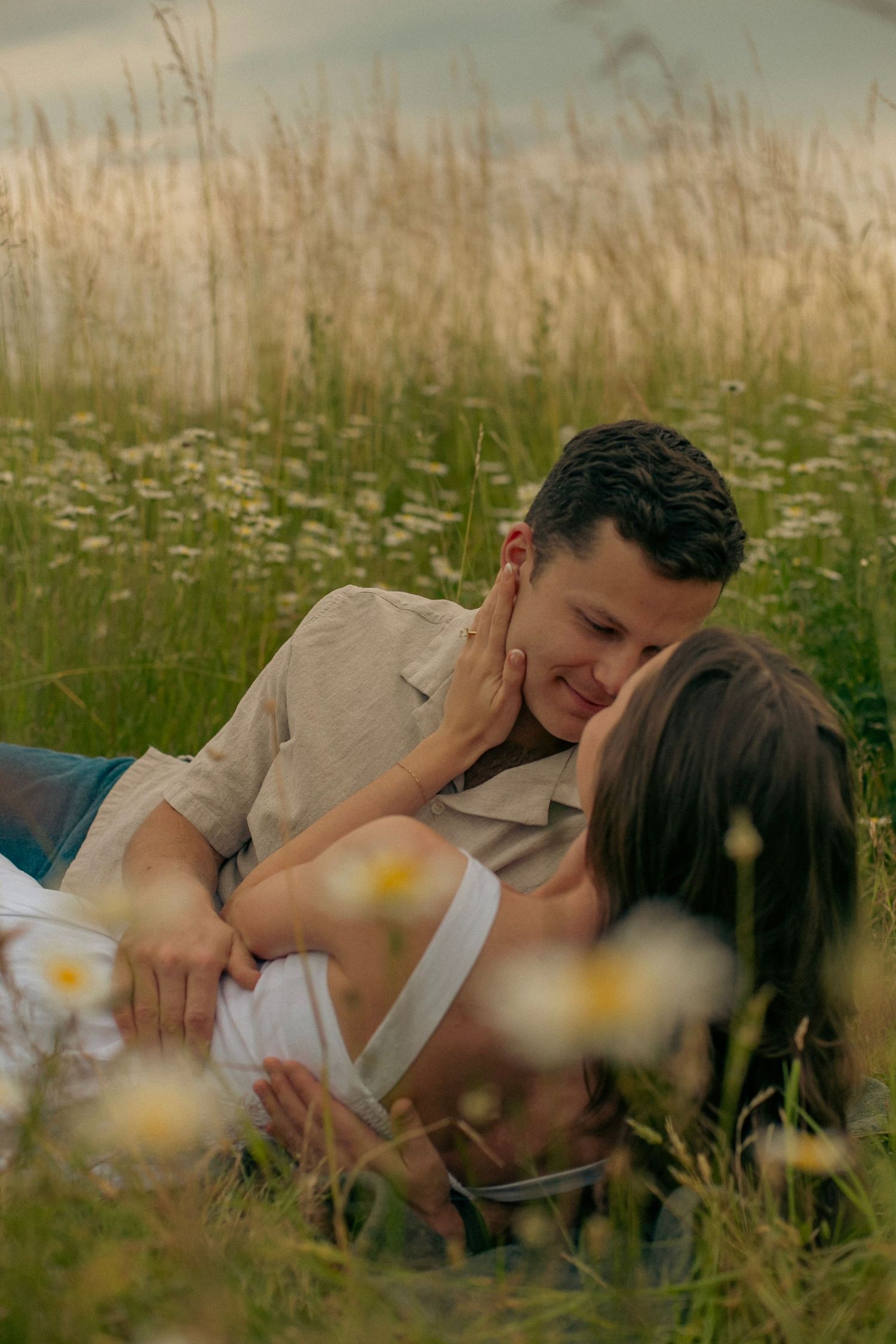 A man and woman laying in a field of wildflowers, the man looking longingly into the woman's eyes.