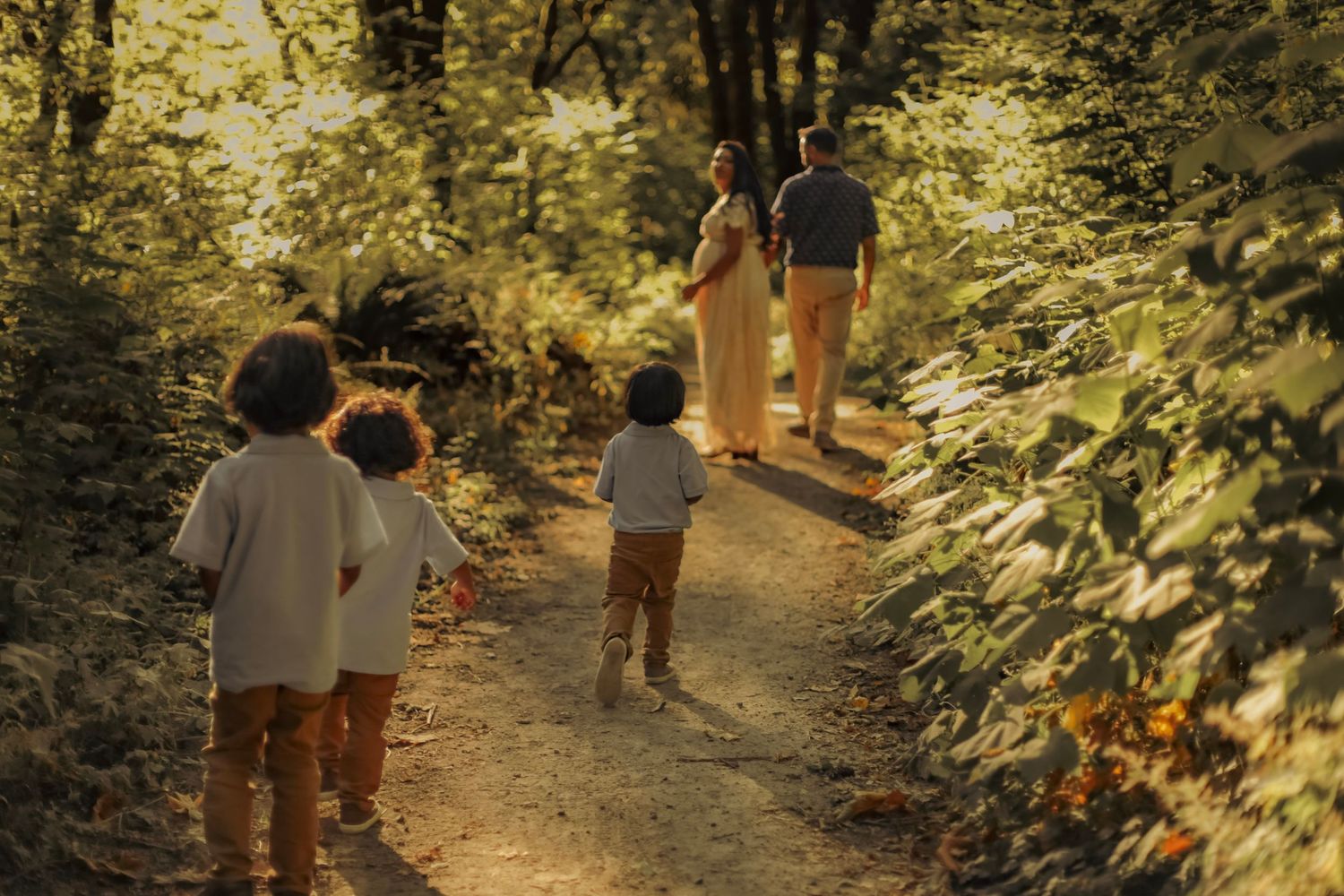 A cute, playful photo of three young boys running after their parents on a woodland trail in the forest.