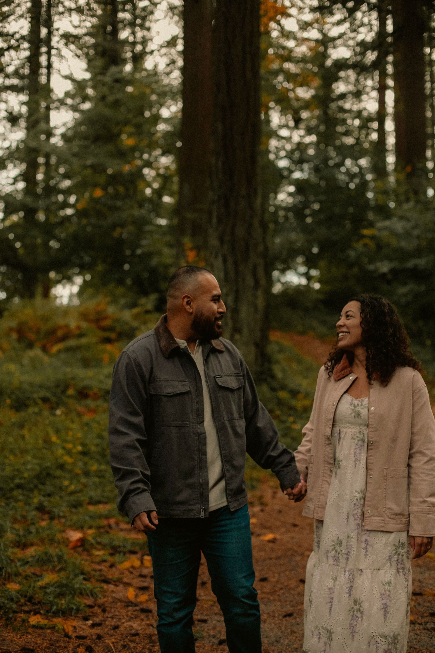 Couple holding hands and smiling at each other while walking in the forest in Oregon for engagement photos