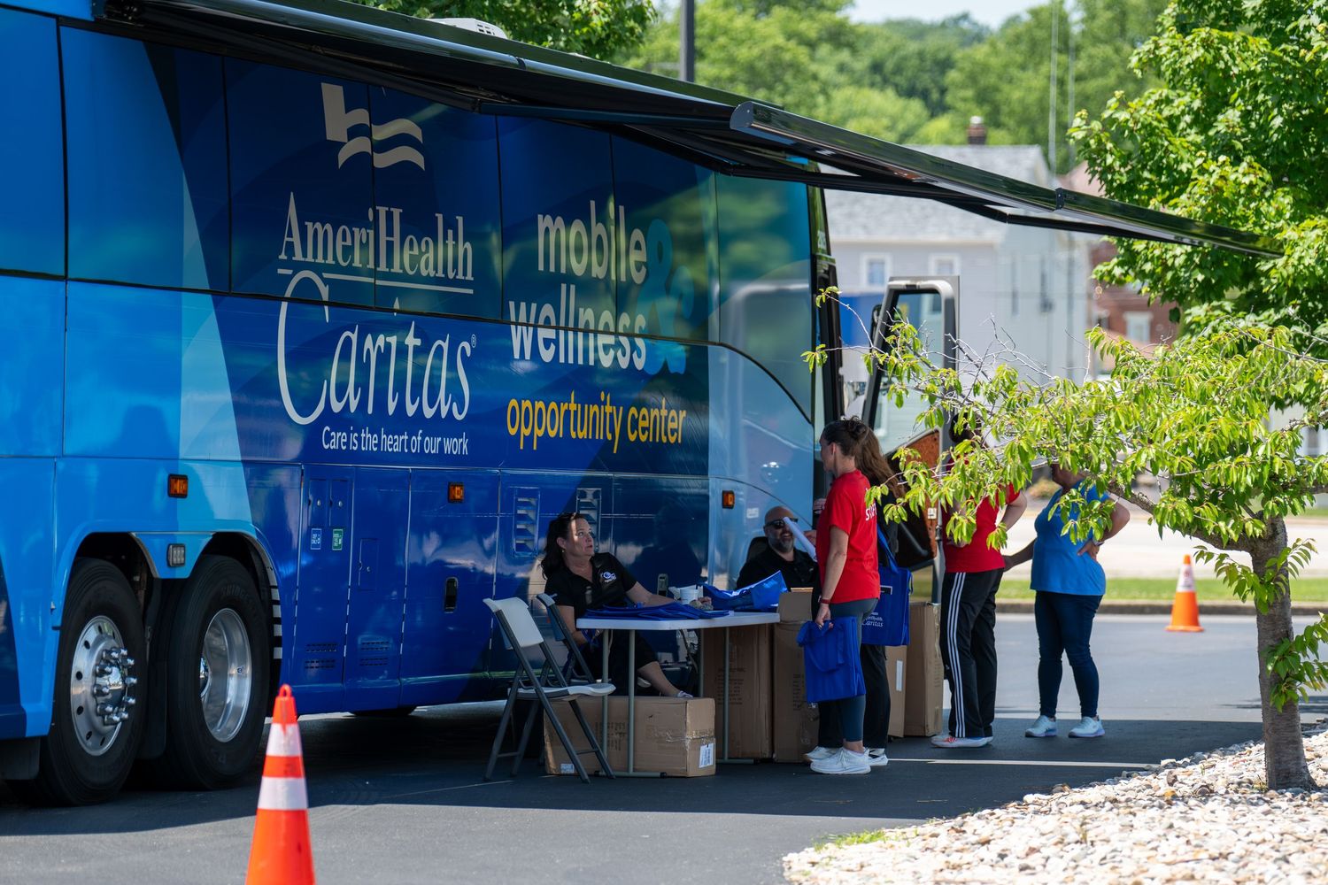 AmeriHealth Caritas mobile wellness opportunity center bus with staff assisting community members outdoors.