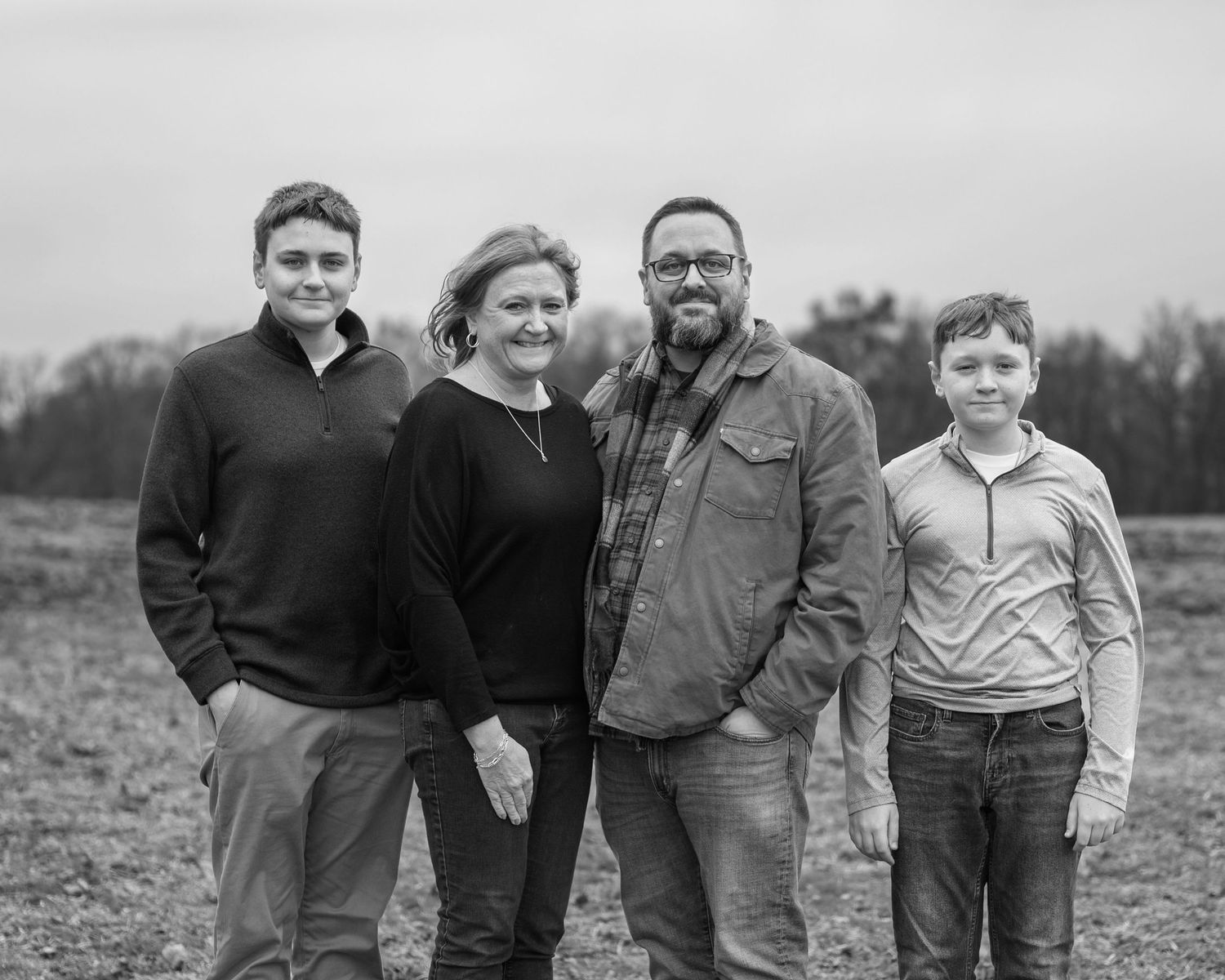 Black and white family portrait of The Hanke Family standing together in an open field outdoors.
