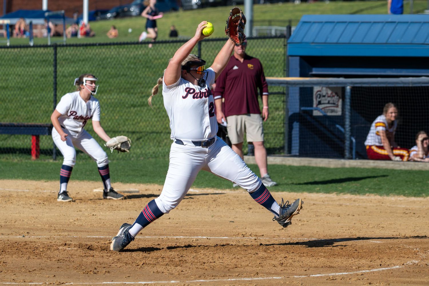 Softball pitcher in navy uniform mid-windup on sunny field during competitive game.