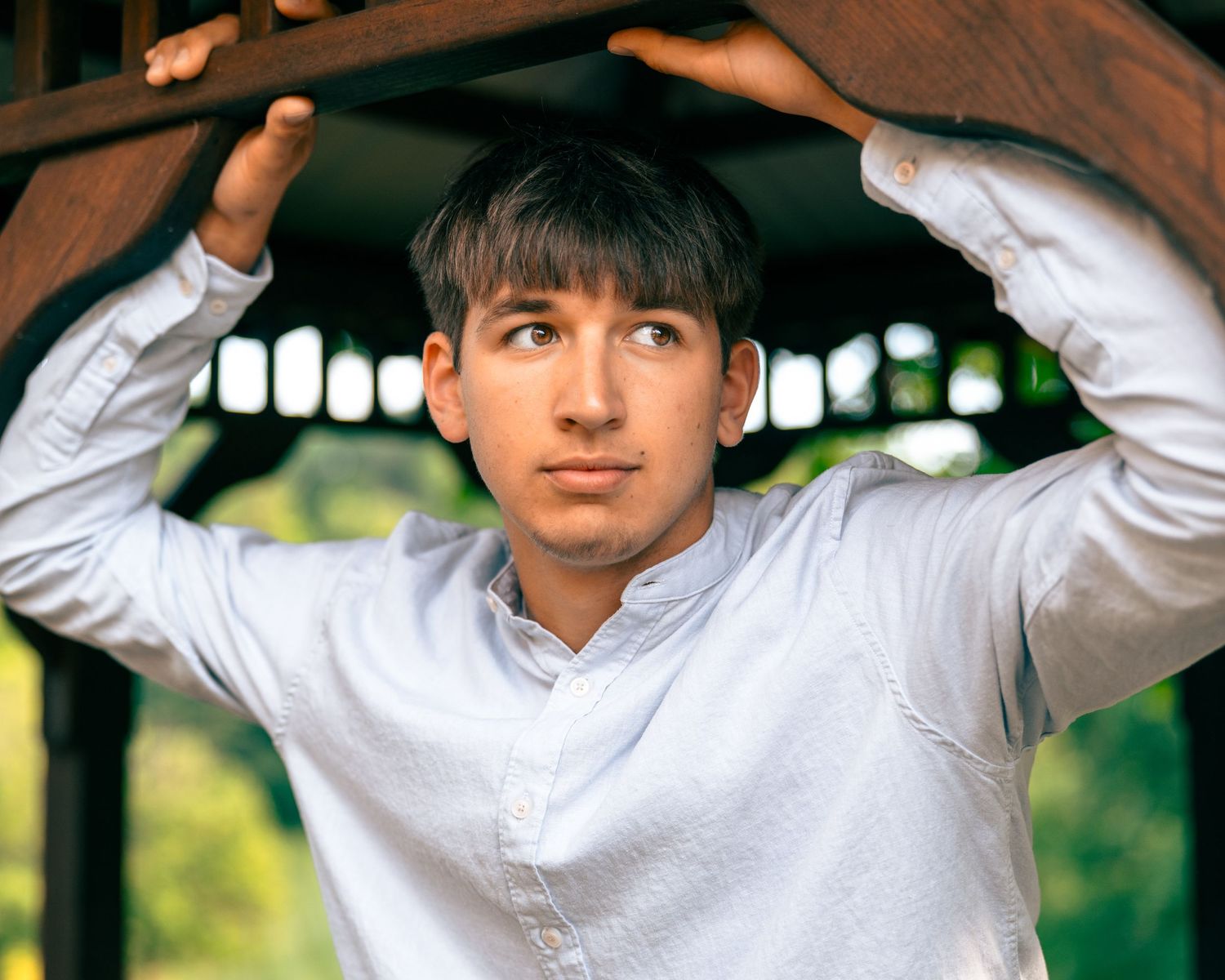 Young man in white shirt holding wooden gazebo frame overhead outdoors.