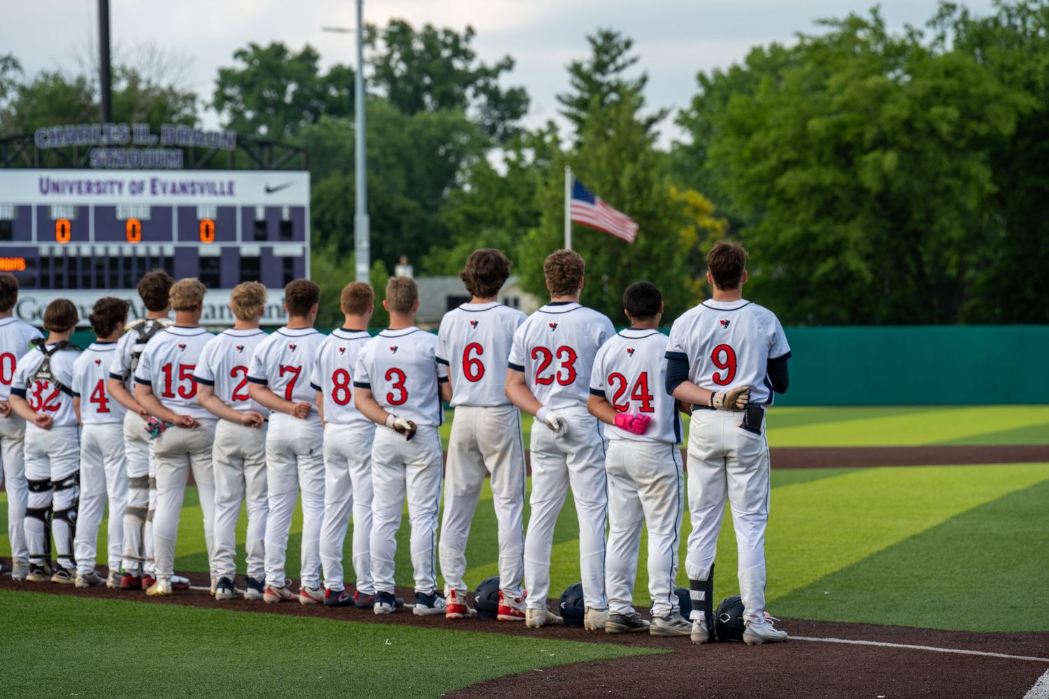 Baseball team lined up on field at University of Evansville stadium during national anthem with American flag.