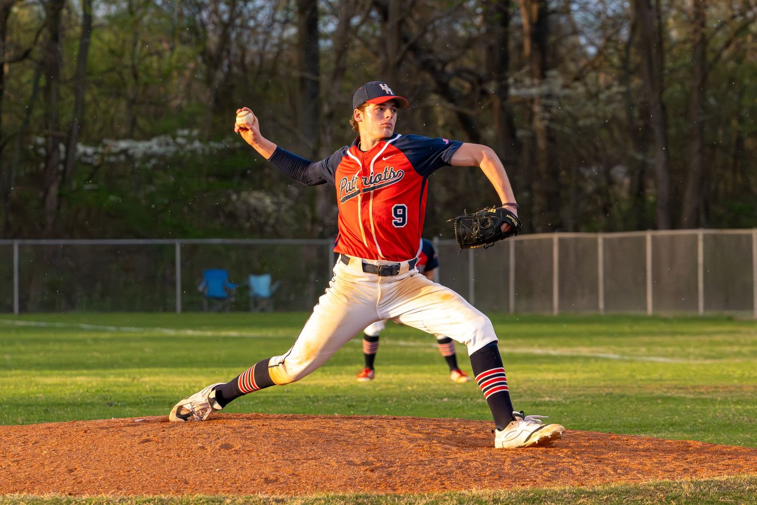 Baseball pitcher in orange and white uniform number 9 winds up for a pitch on a sunny day at a green field.