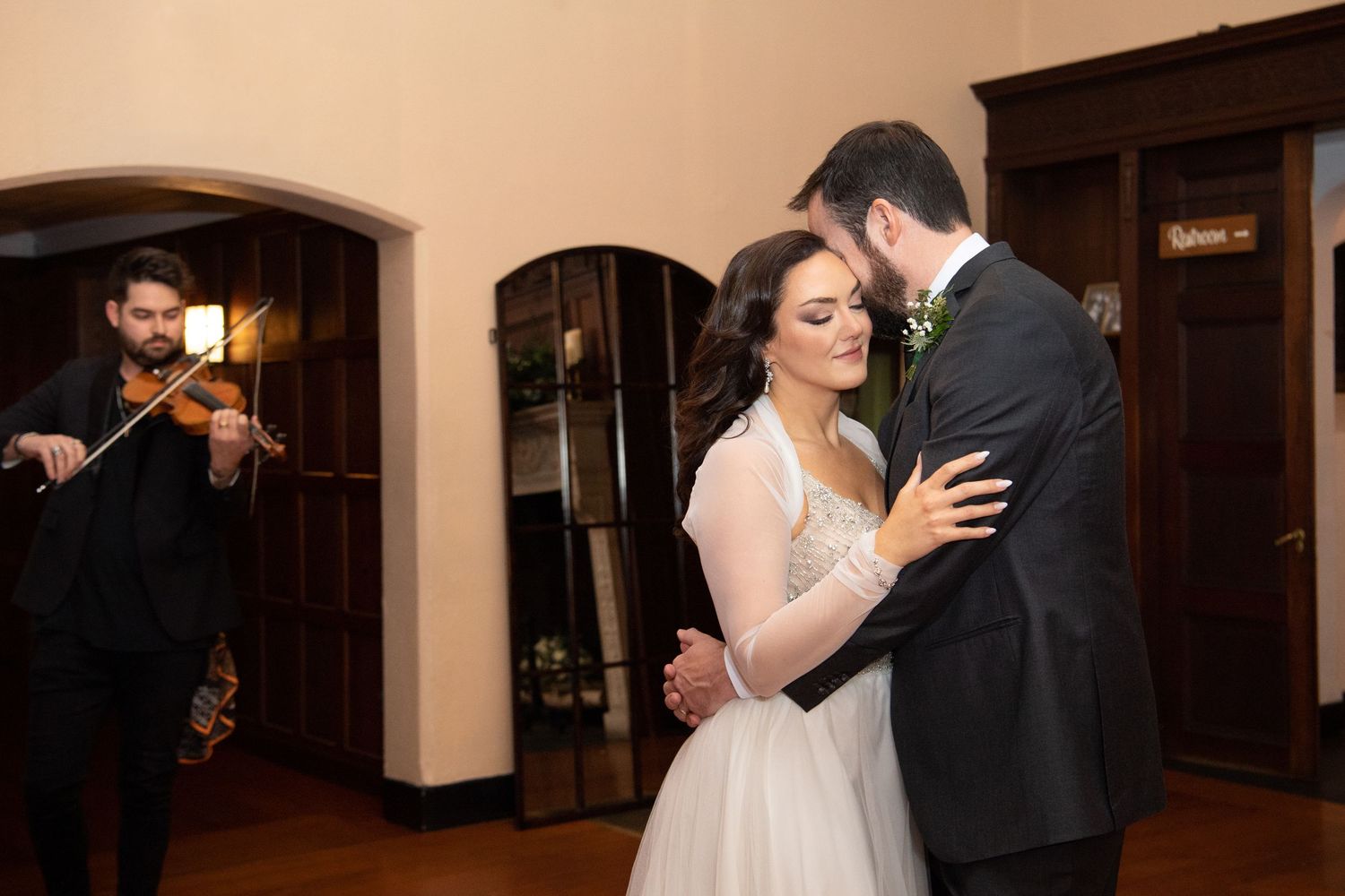 A couple dances together during their wedding reception in a dimly lit venue.