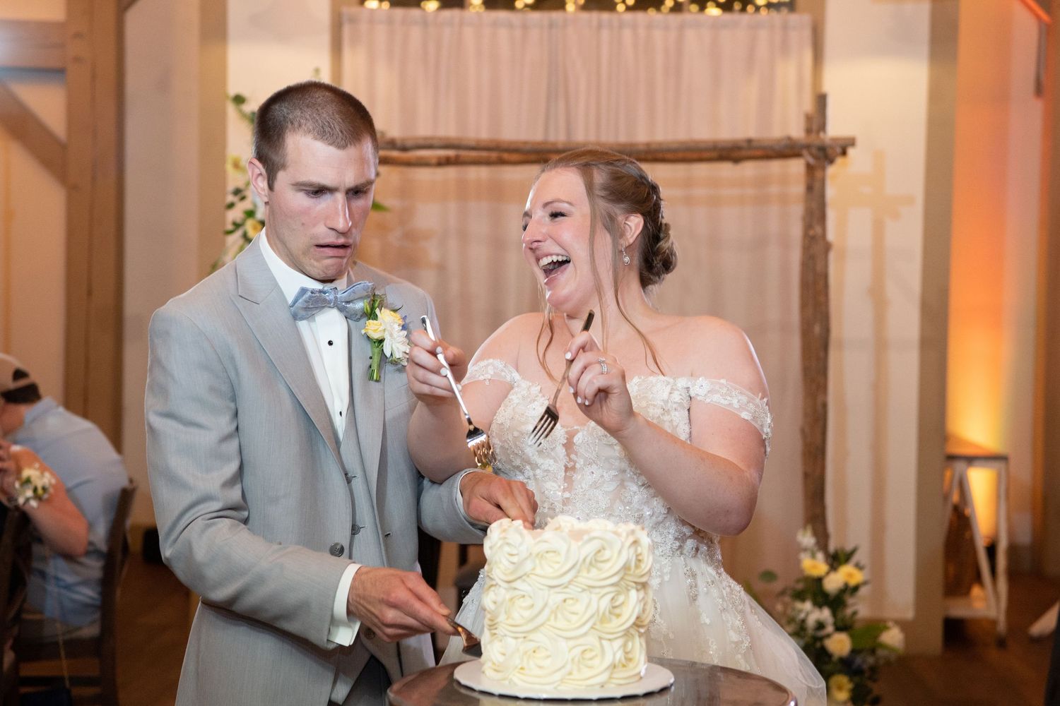 Newlyweds feeding each other bites of wedding cake in a decorated reception venue at the reception celebration.