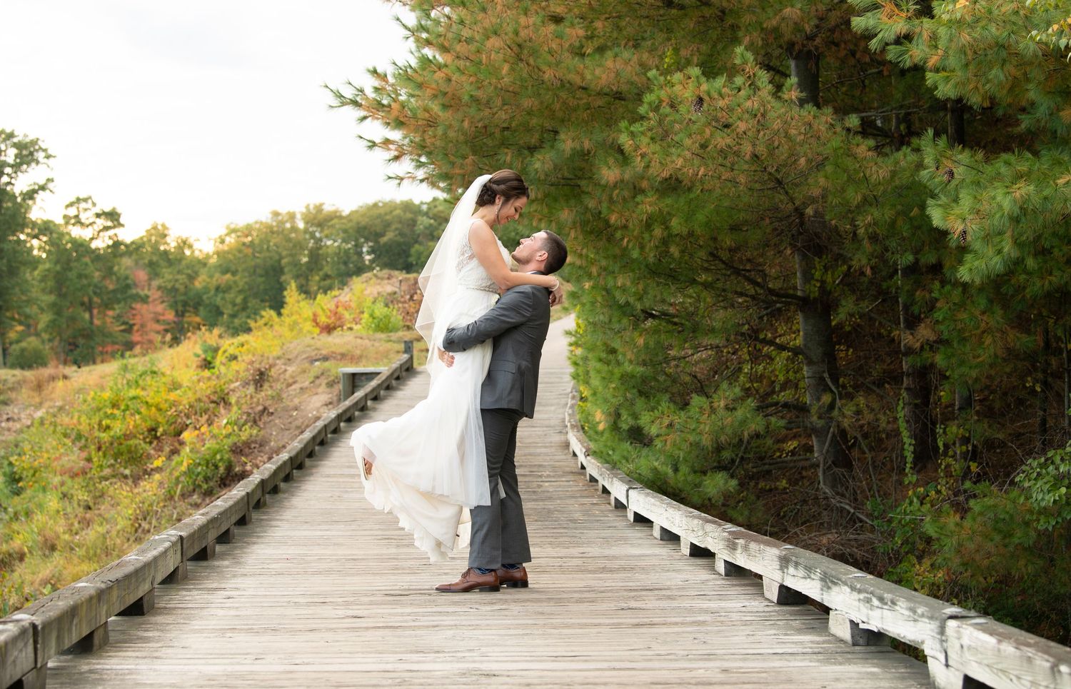 Romantic fall wedding photos with couple posing in series of romantic poses on wooden bridge walkway.