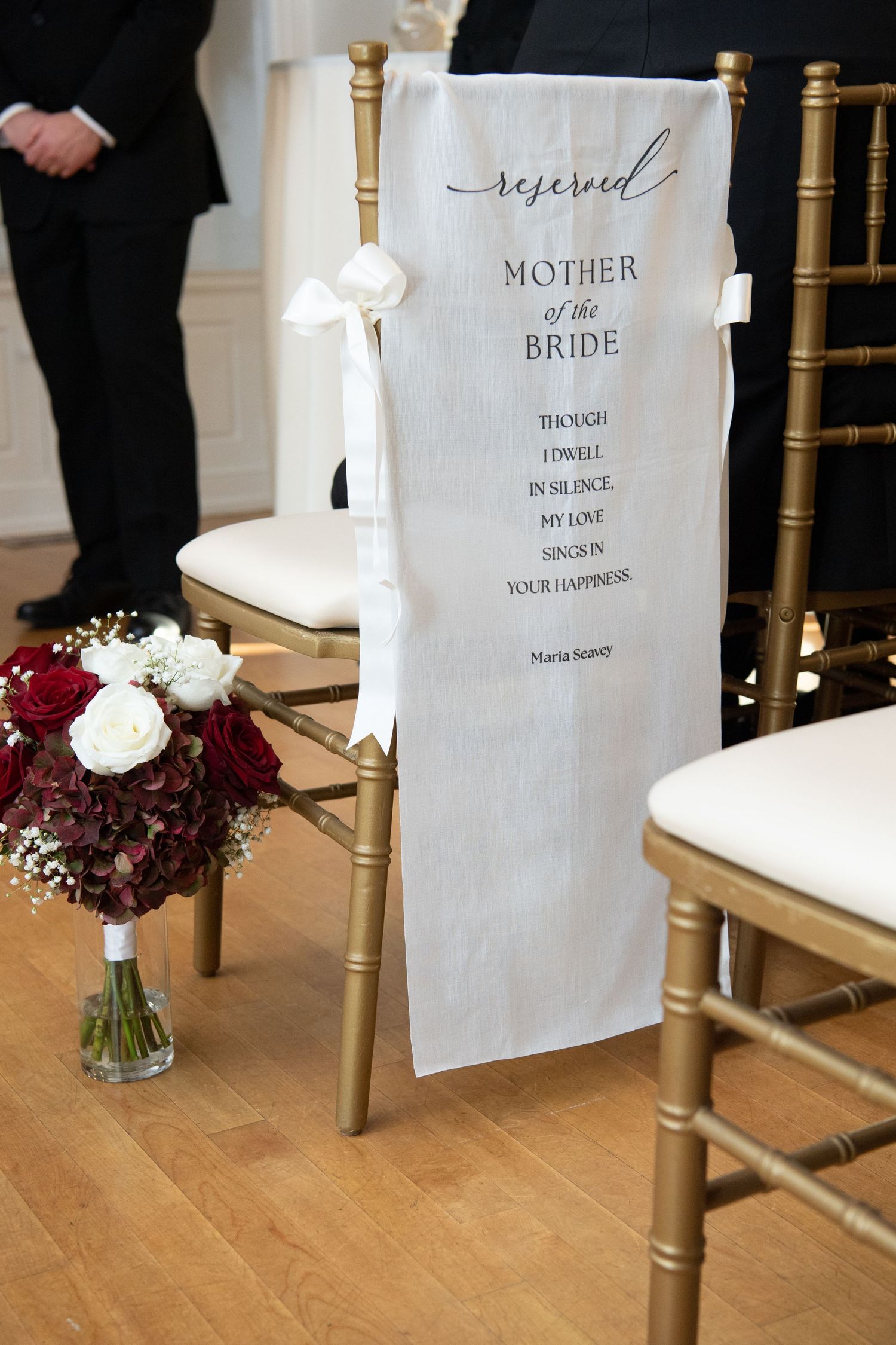 Reserved seating signs and burgundy floral arrangements next to gold chiavari chairs at a wedding ceremony.