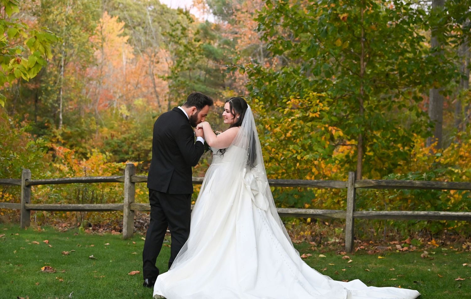 A couple in wedding attire shares romantic moments in a scenic autumn garden with vibrant fall foliage.