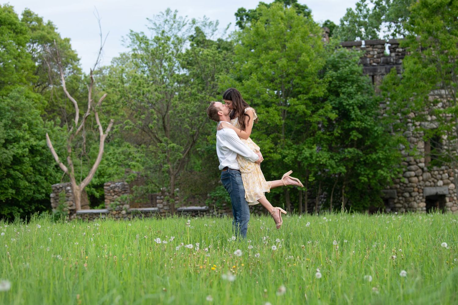 Person dancing joyfully in a green meadow with wildflowers and trees in the background.