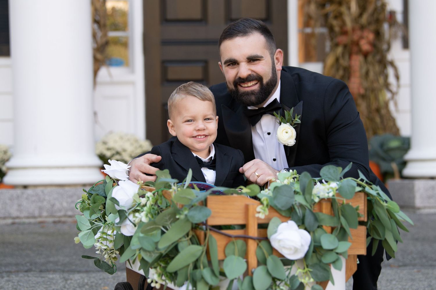 A festive fall wedding scene on a white columned porch with greenery and seasonal decorations.