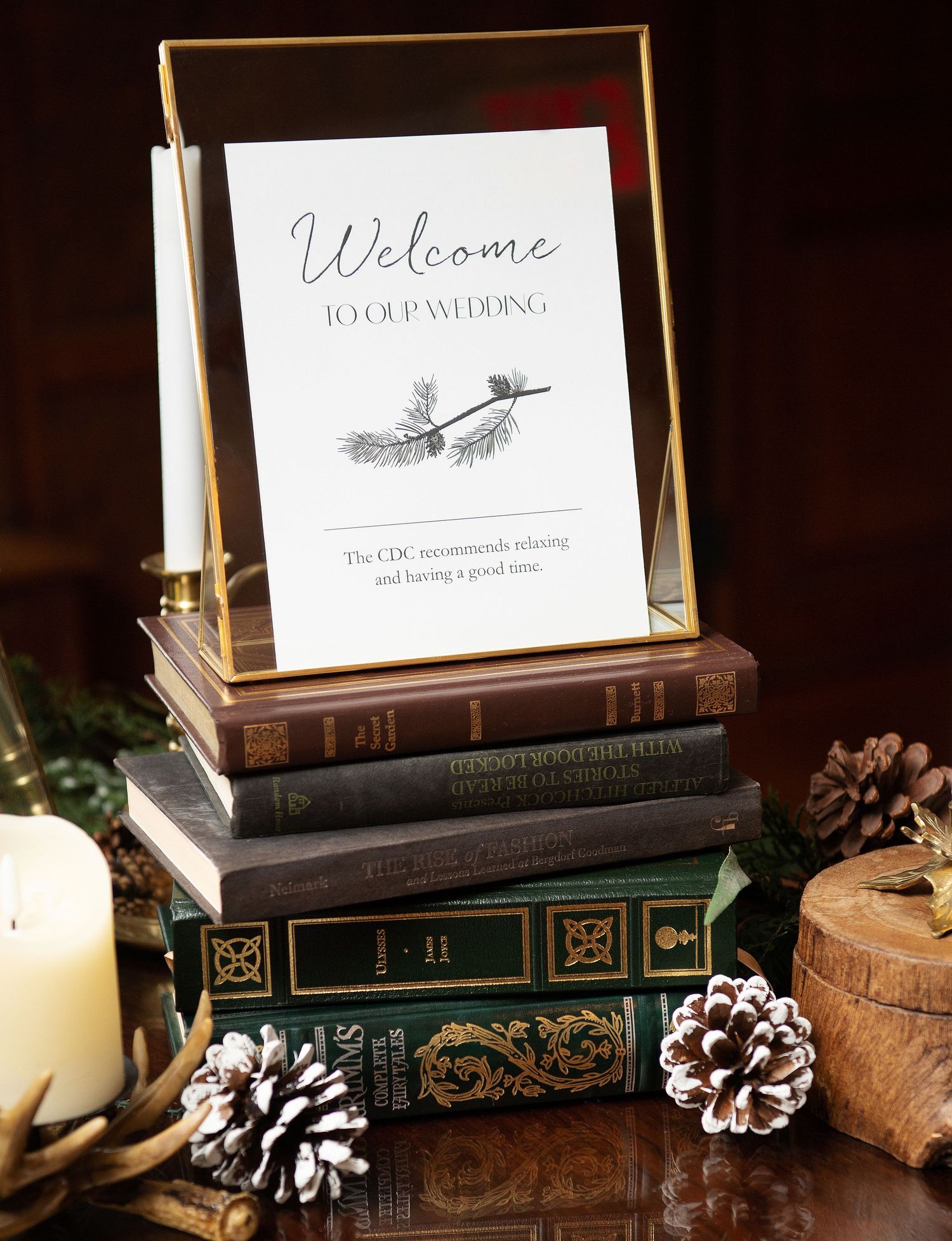 Vintage books with welcome signs and decorative pinecones arranged on a dark wooden surface.