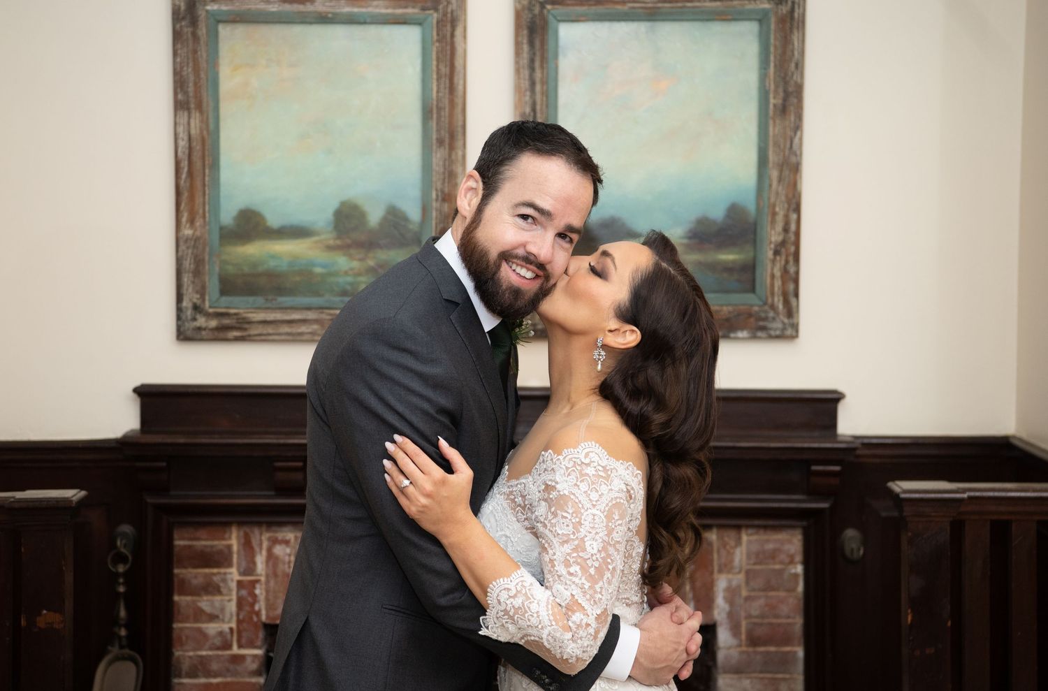A bride and groom share a joyful embrace while laughing together in an elegant indoor setting with artwork on the walls.