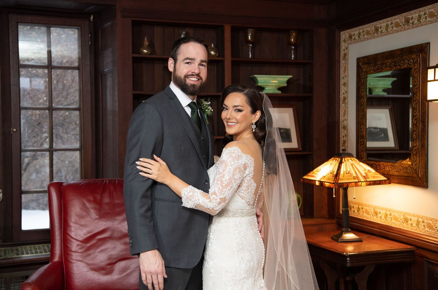 A newlywed couple poses together in an intimate indoor setting with vintage decor and warm lighting.