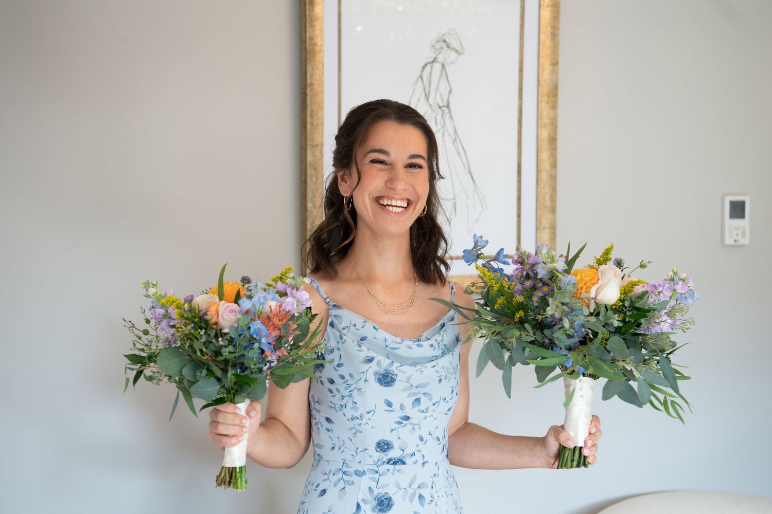 Bridesmaid in a blue floral dress holds two colorful summer bouquets with wildflowers and greenery.