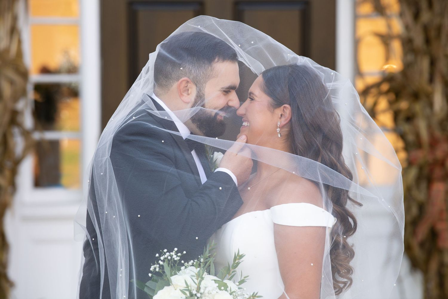 A romantic wedding couple shares a kiss during golden hour while standing outdoors in formal attire.