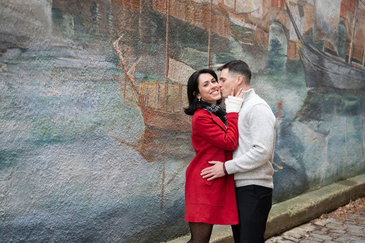 A couple shares romantic moments in an outdoor setting with stone walls and natural lighting.