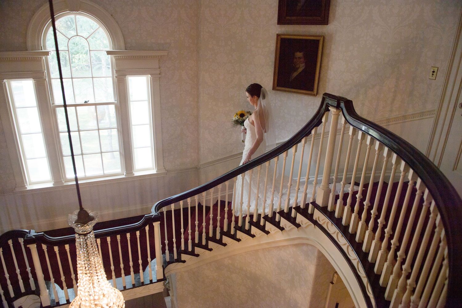 Elegant curved wooden banister along a grand staircase in an upscale interior with multiple windows providing natural light.