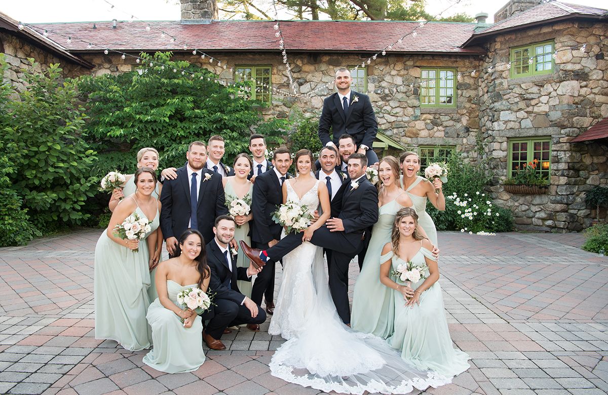 A wedding party poses for panoramic photos on a beautiful stone patio with garden views in the background.