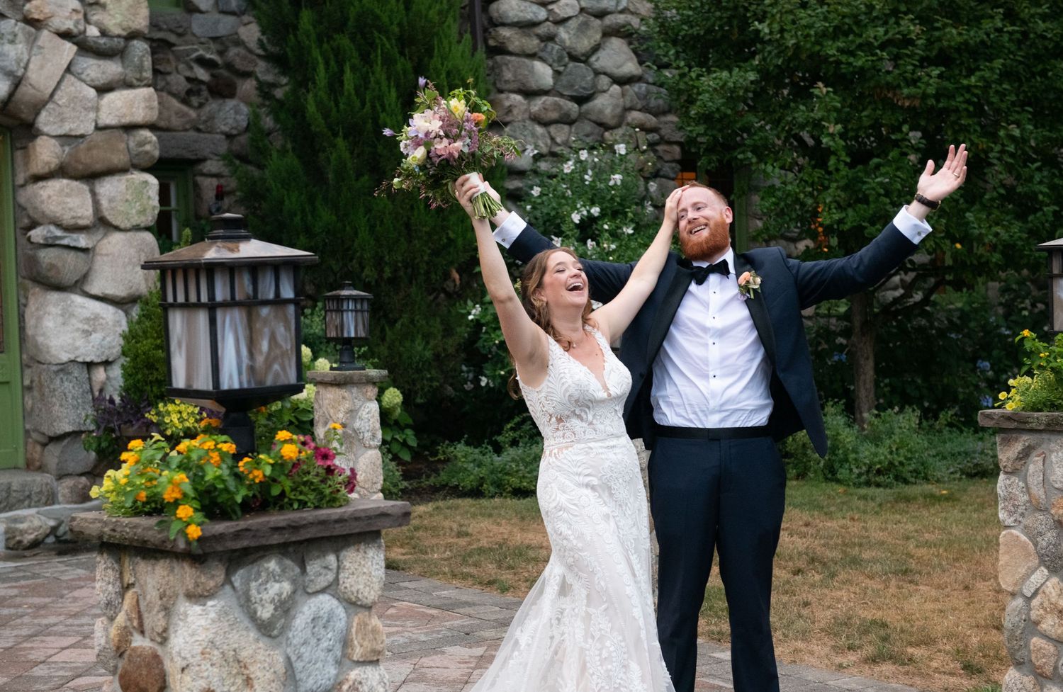 Wedding couple dancing and celebrating on stone patio surrounded by greenery.