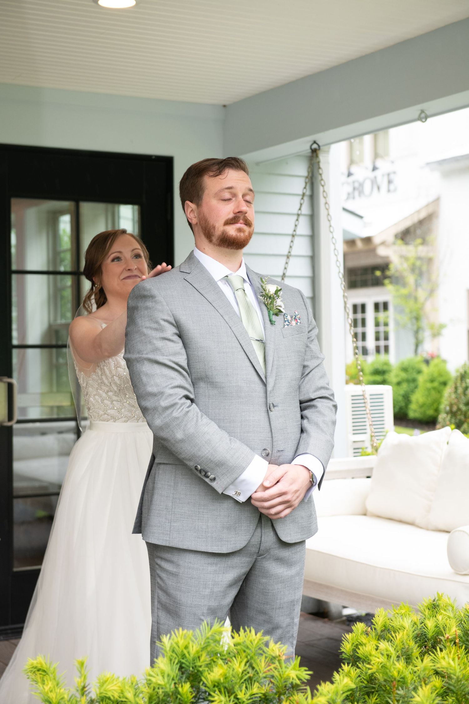 First look wedding photos on a porch with couple in grey suit and white dress.
