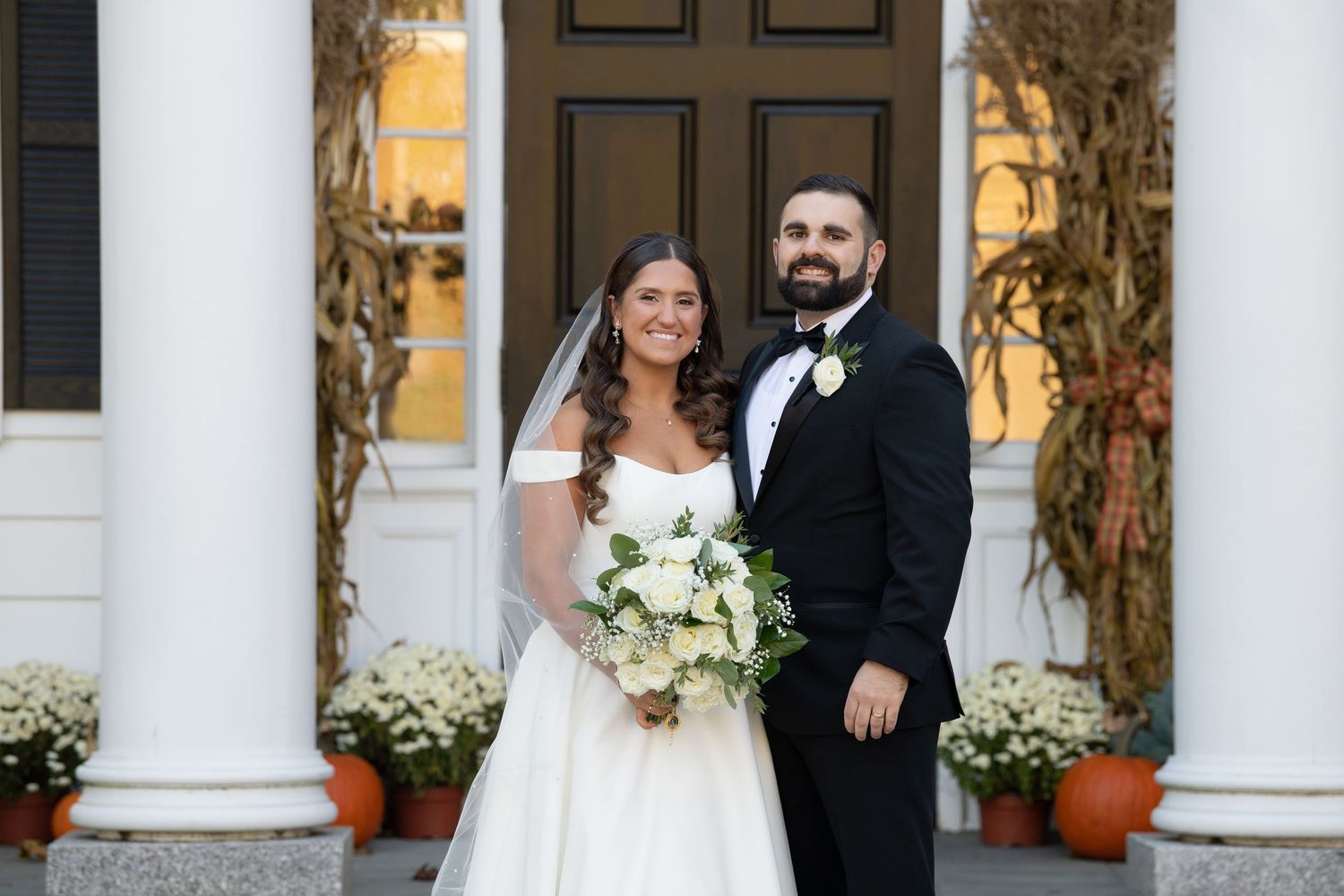 A wedding couple poses together outdoors in front of white columns at an elegant venue during their special day.