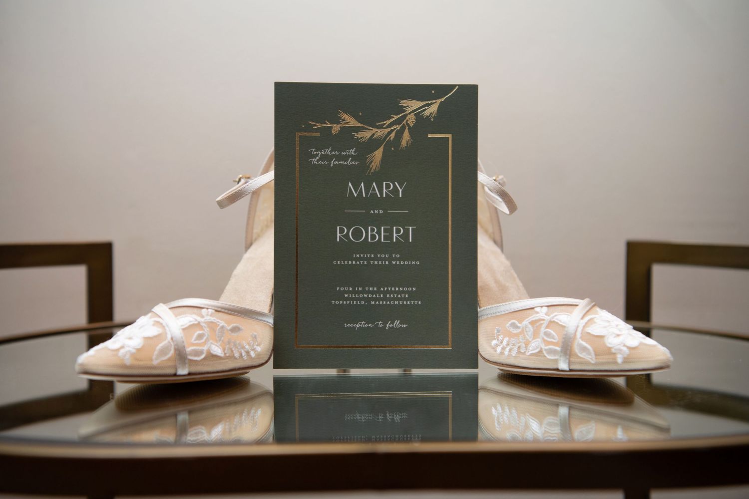 Elegant wedding invitation cards in dark green displayed alongside white bridal shoes on a reflective surface.