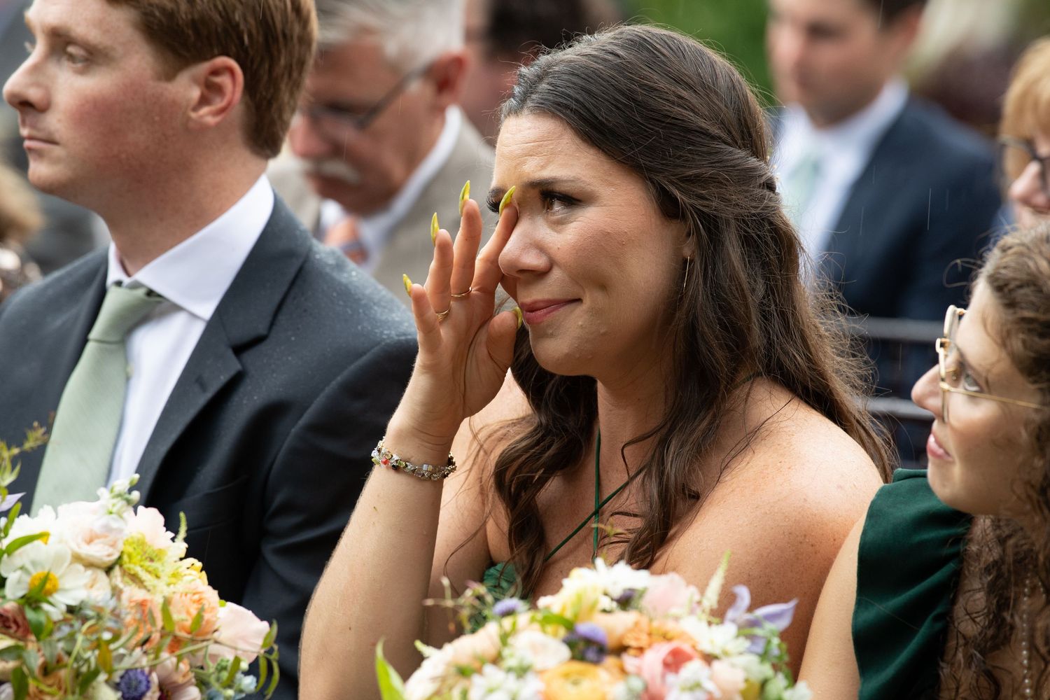Wedding guest wiping tears during an emotional outdoor ceremony.