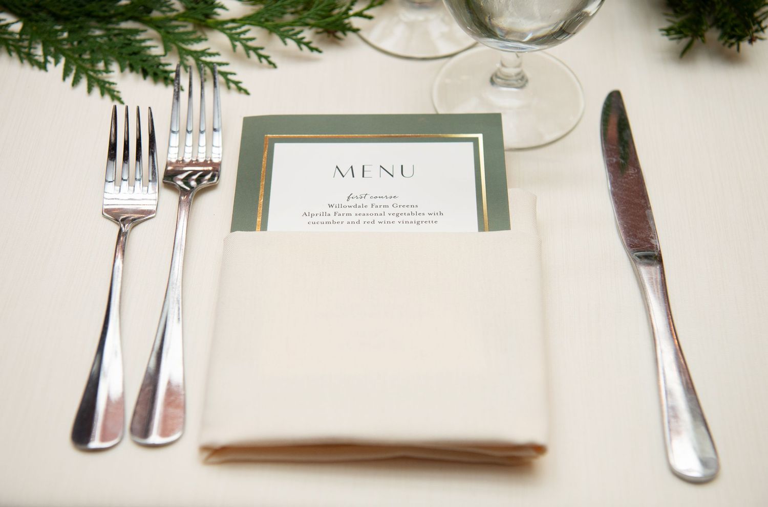 Elegant place setting with silverware, white napkin and menu card decorated with evergreen sprigs.