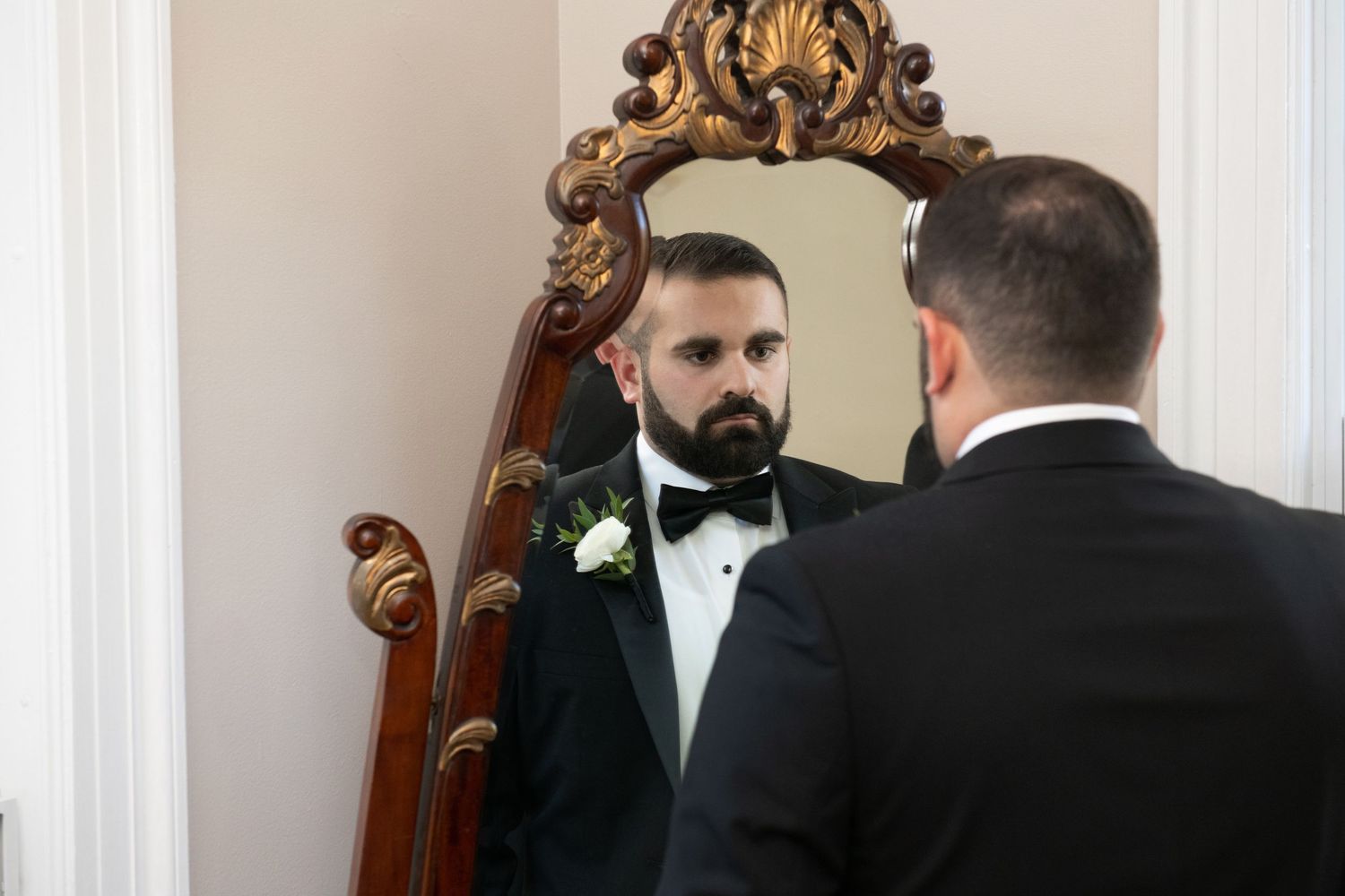 A group of formally dressed people gather in an elegant room with ornate mirrors and decorative moldings.