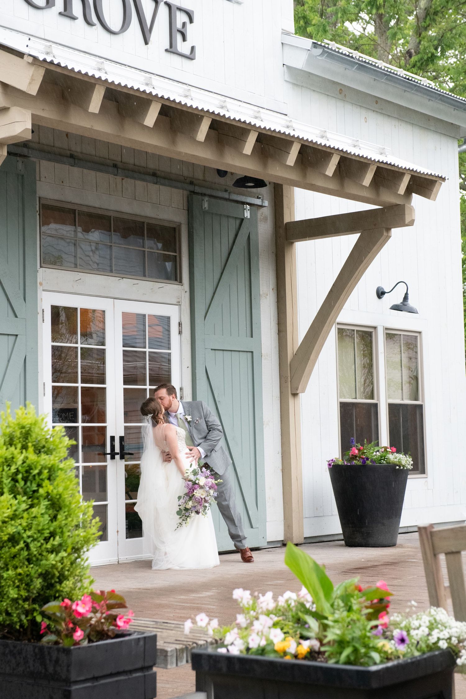 White wedding venue exterior features blue shutters, wooden beams, and decorative flower planters along the porch.