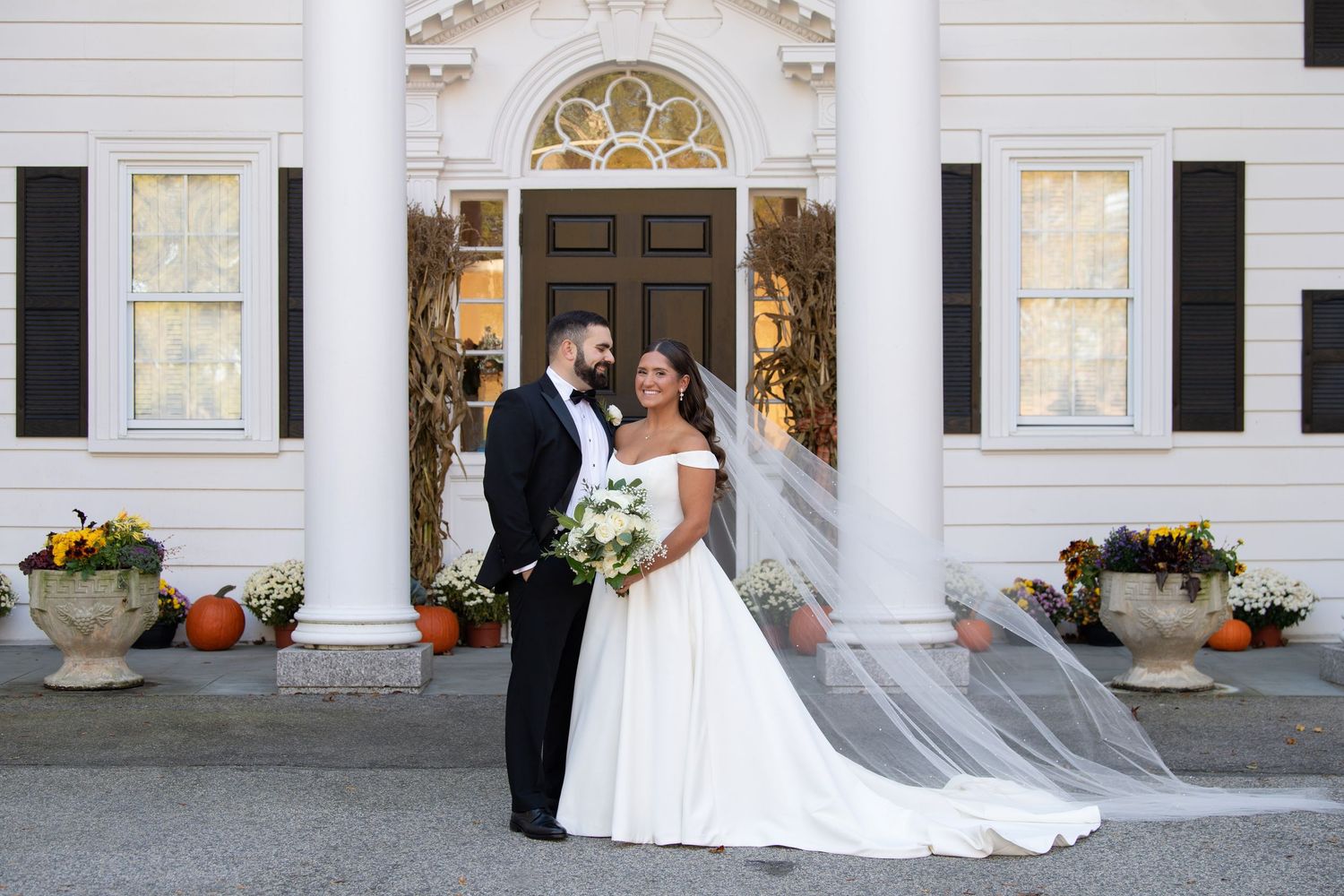 A couple in formal wedding attire poses for photos in front of a white building with elegant columns.