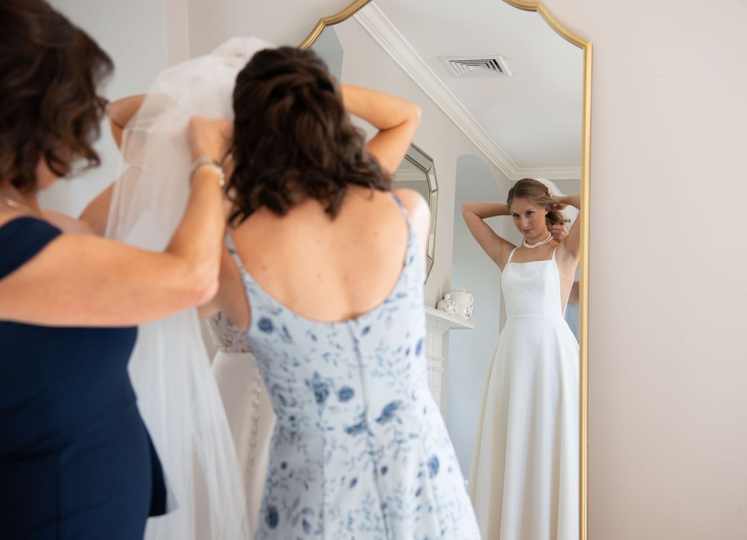 A series of photos showing someone being helped into a delicate white floral wedding dress.