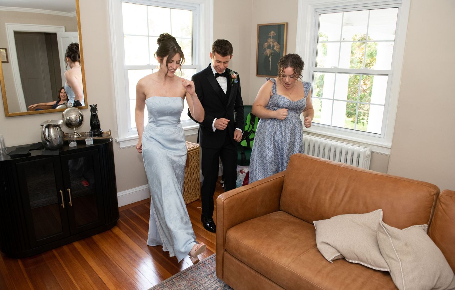 Wedding preparations in a bright sunlit room with a brown leather couch.