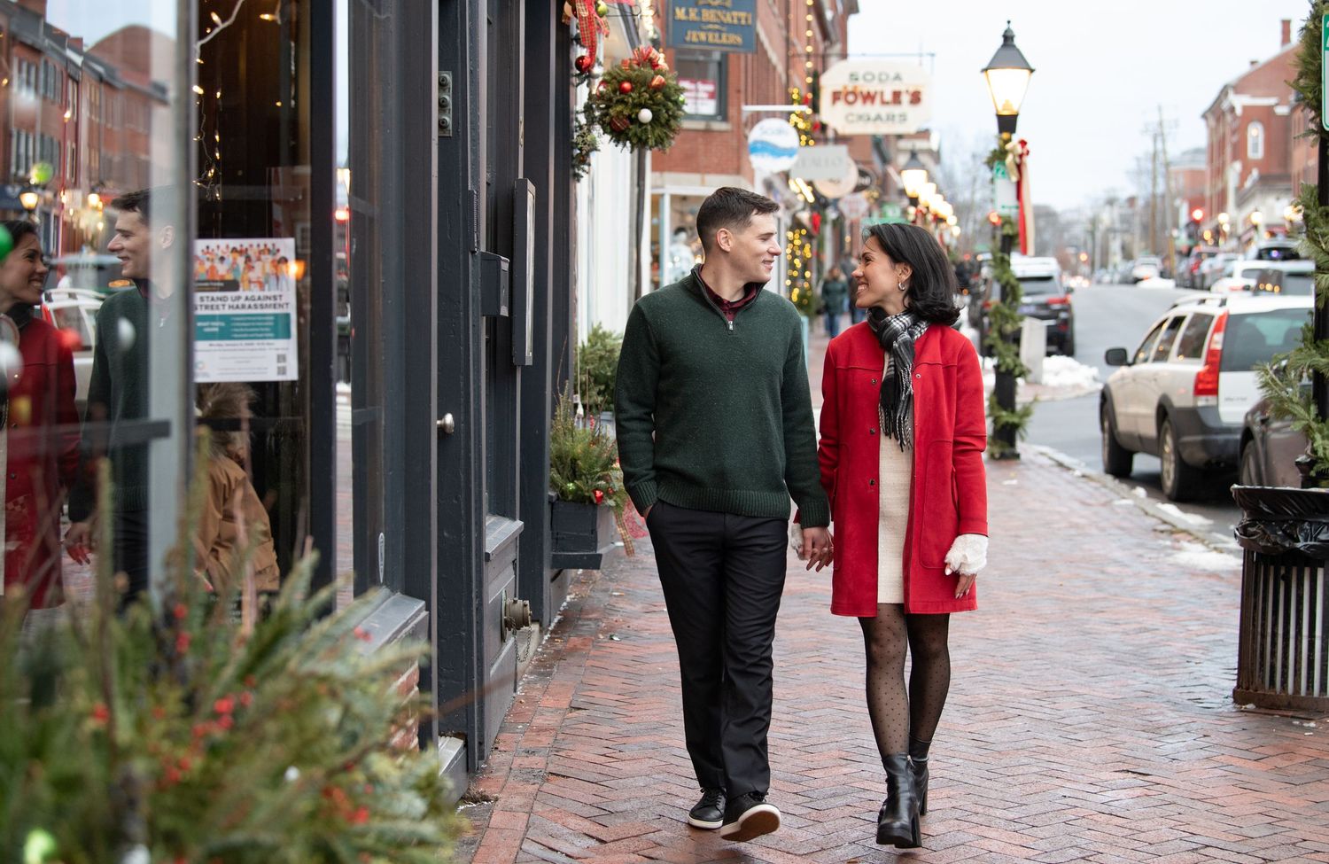 People walking on a brick sidewalk in a historic downtown area during winter with storefronts and holiday decorations.