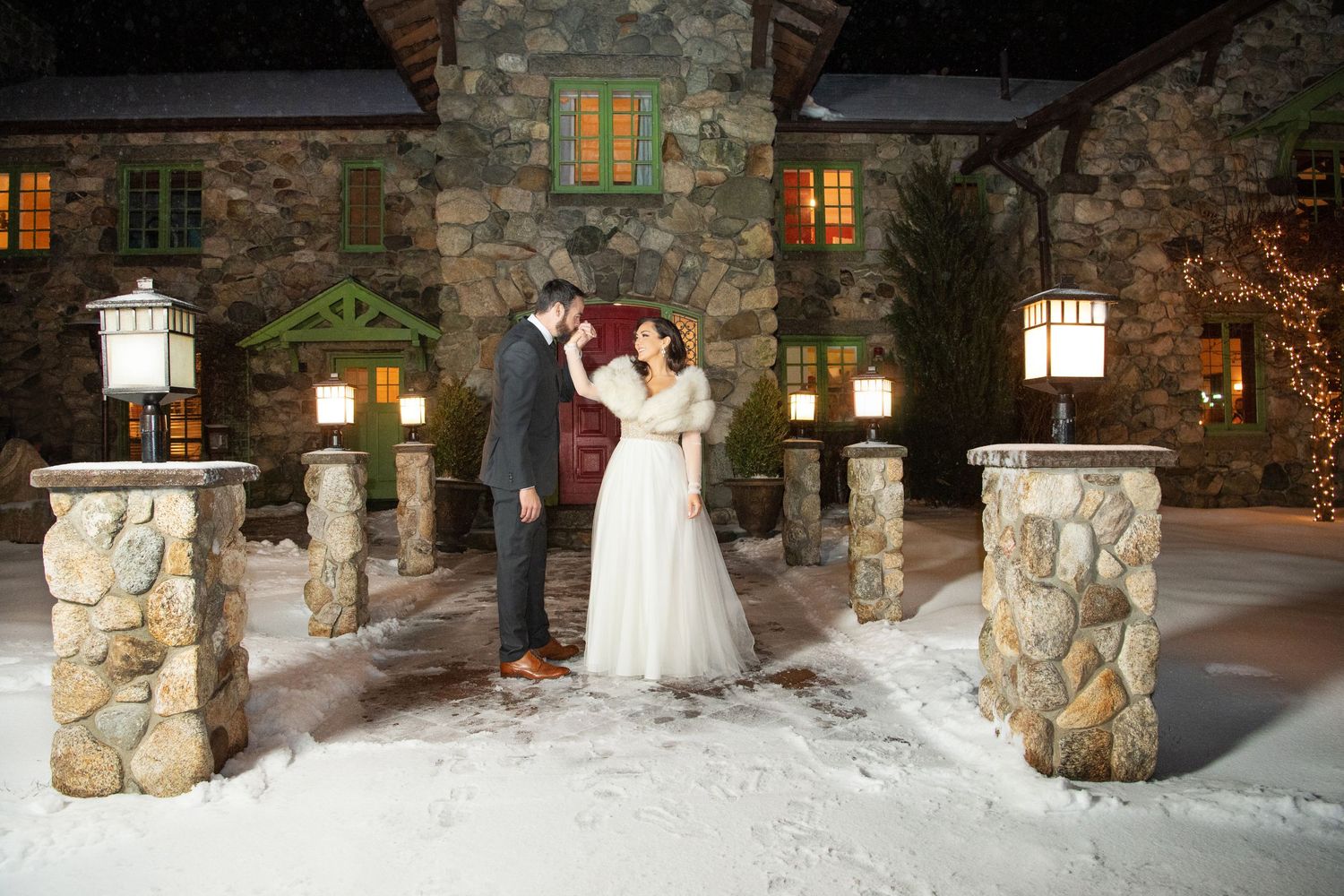 Panoramic winter wedding scene with illuminated stone pillars and snow-covered grounds at a rustic venue.