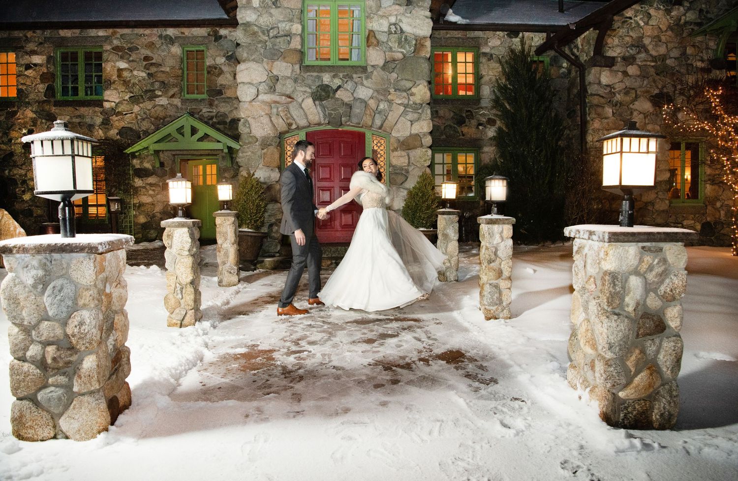 Snow-covered stone pillars and lanterns line a rustic pathway at night.