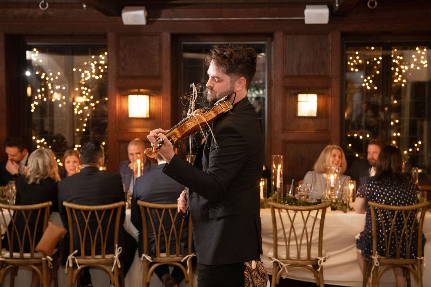 Guests enjoy a romantic evening reception with string lights and lanterns in a rustic wooden venue.