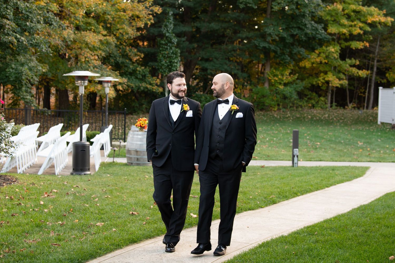 Wedding party members in black suits walk down an outdoor path during a fall ceremony.